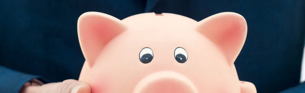 A person in a dark blue suit holds a pink piggy bank with both hands.