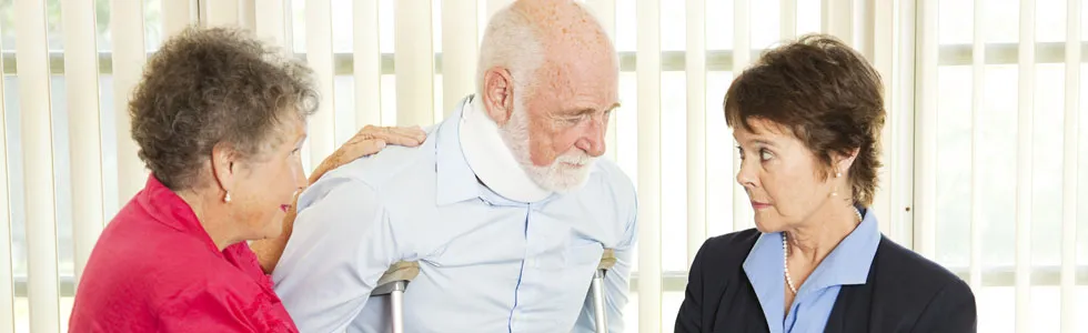 An elderly man with a neck brace and crutches is assisted by two women, one in a red top and one in a blue blazer, in a brightly lit room.