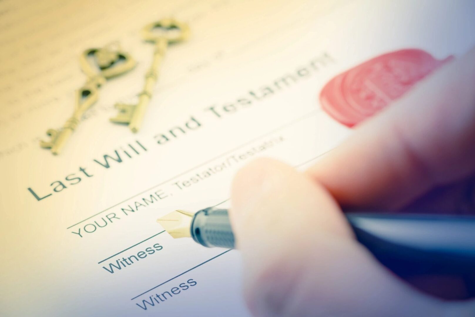 Close-up of a hand holding a pen, signing a "Last Will and Testament" document. There are two blank witness signature lines and a set of old-fashioned keys in the background.