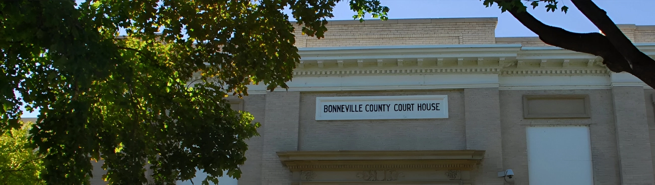 The facade of Bonneville County Courthouse with a sign displaying its name, partially obscured by tree branches.