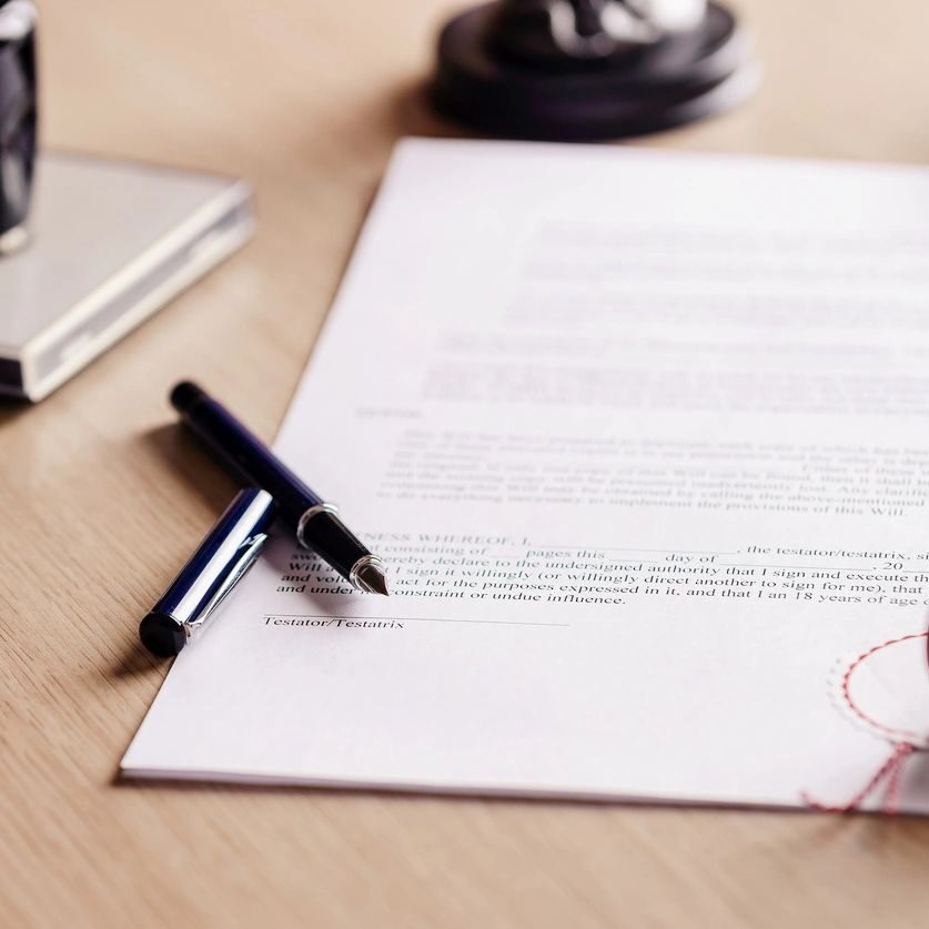 A document on a wooden desk with a fountain pen, ink bottle, red wax seal, and stamp.