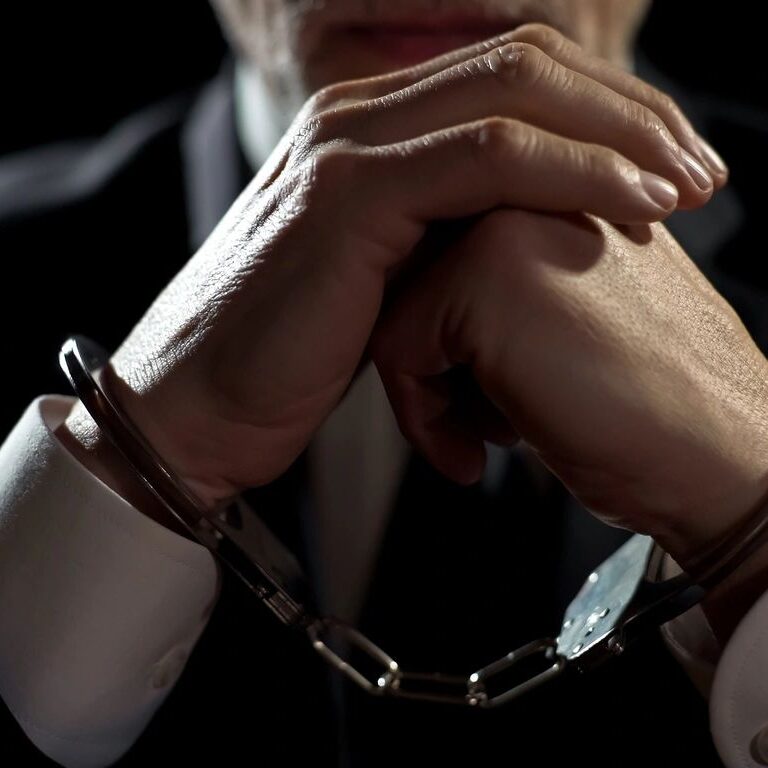 A person in a suit with their hands clasped together, wearing handcuffs.