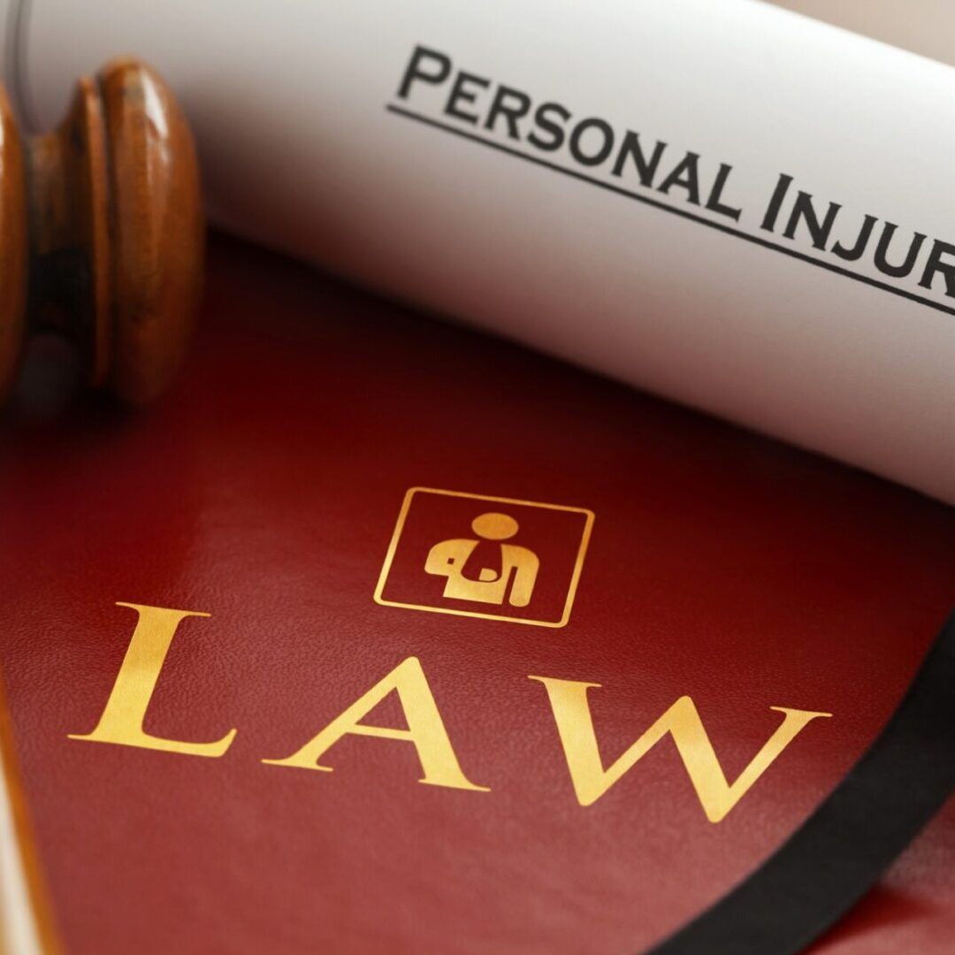 A gavel and a rolled document labeled "Personal Injury" lie on top of a red book with the word "LAW" and a symbol of a person in a suit.